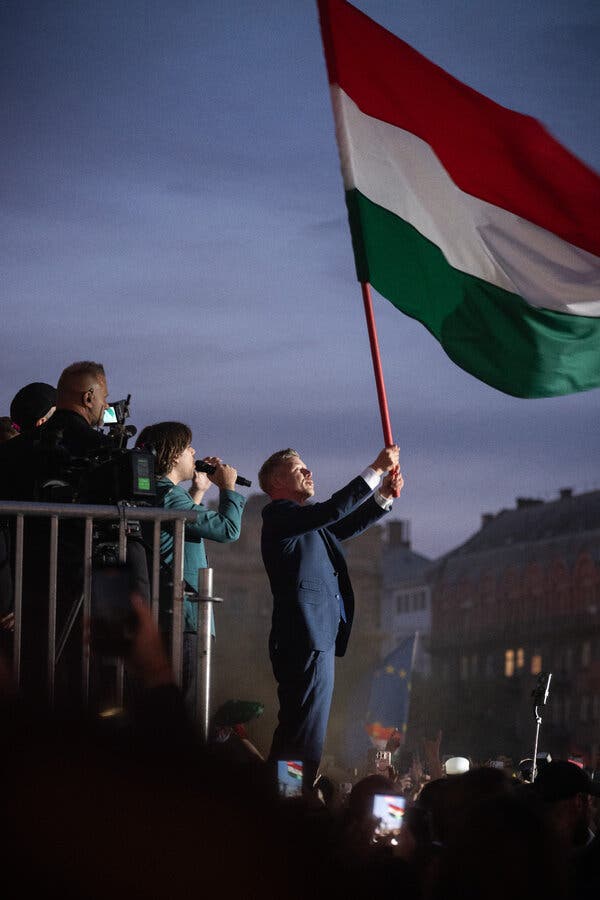 A man in a dark blue suit waves a huge red, white and green flag against a darkening sky.
