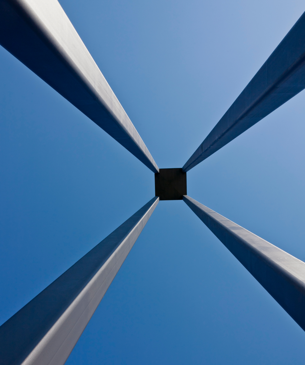 Four tall gray pillars converge at a square platform above against a clear blue sky.