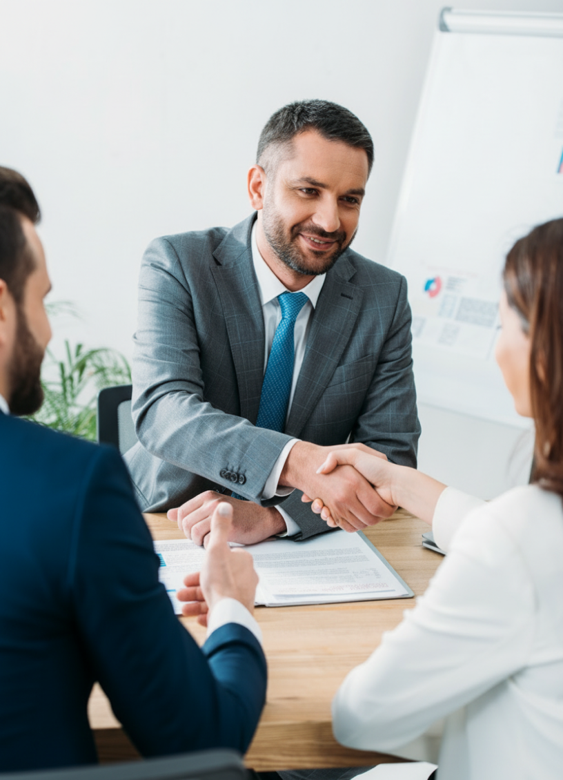 Man in gray suit shaking hands with woman across table during a business meeting.