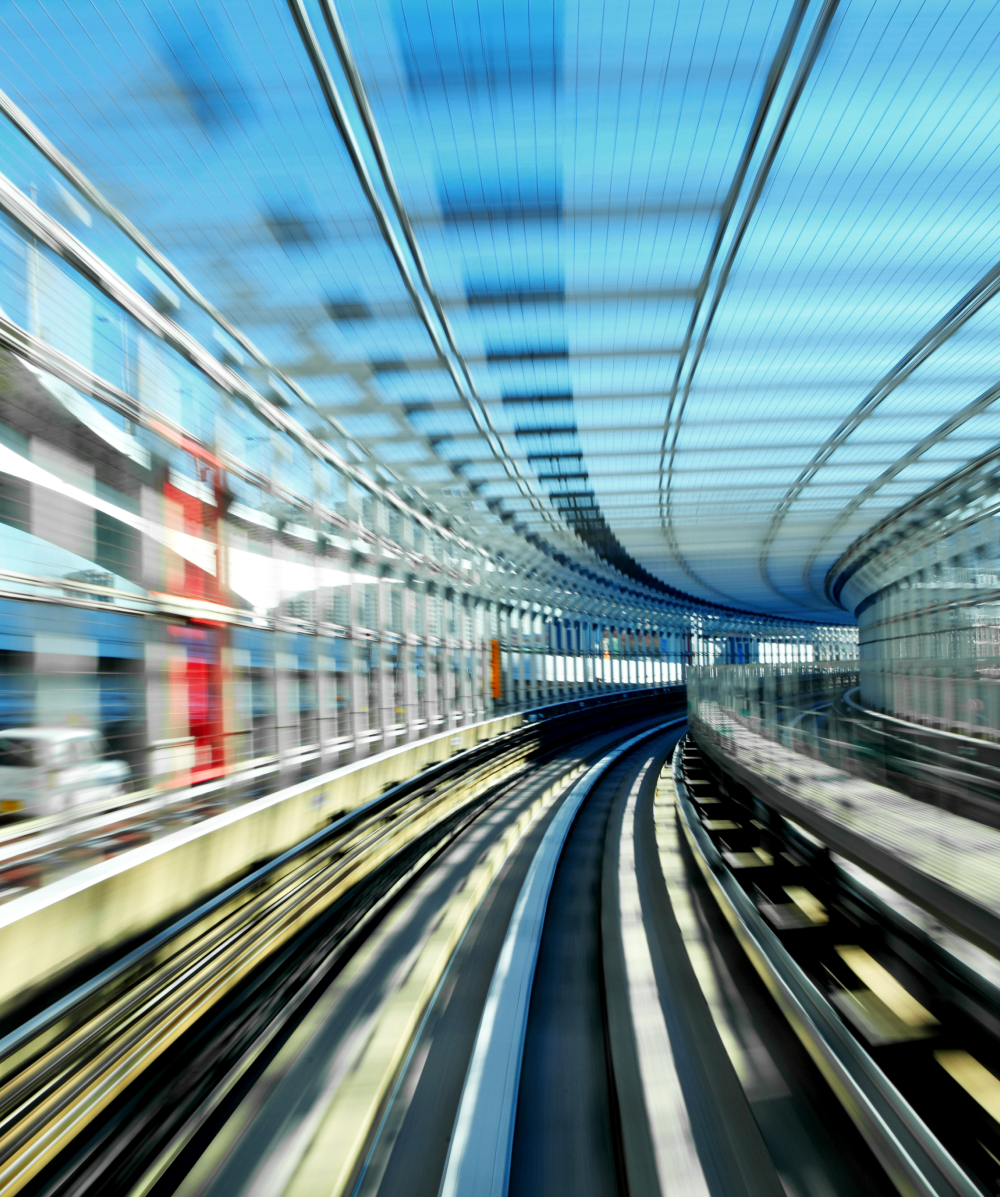 Blurred view of curved elevated train tracks inside a glass-covered modern rail tunnel.