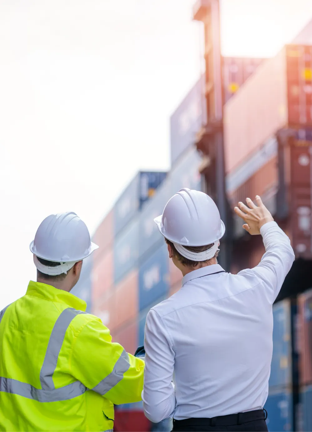 Two workers in safety helmets discussing near stacked shipping containers outdoors.