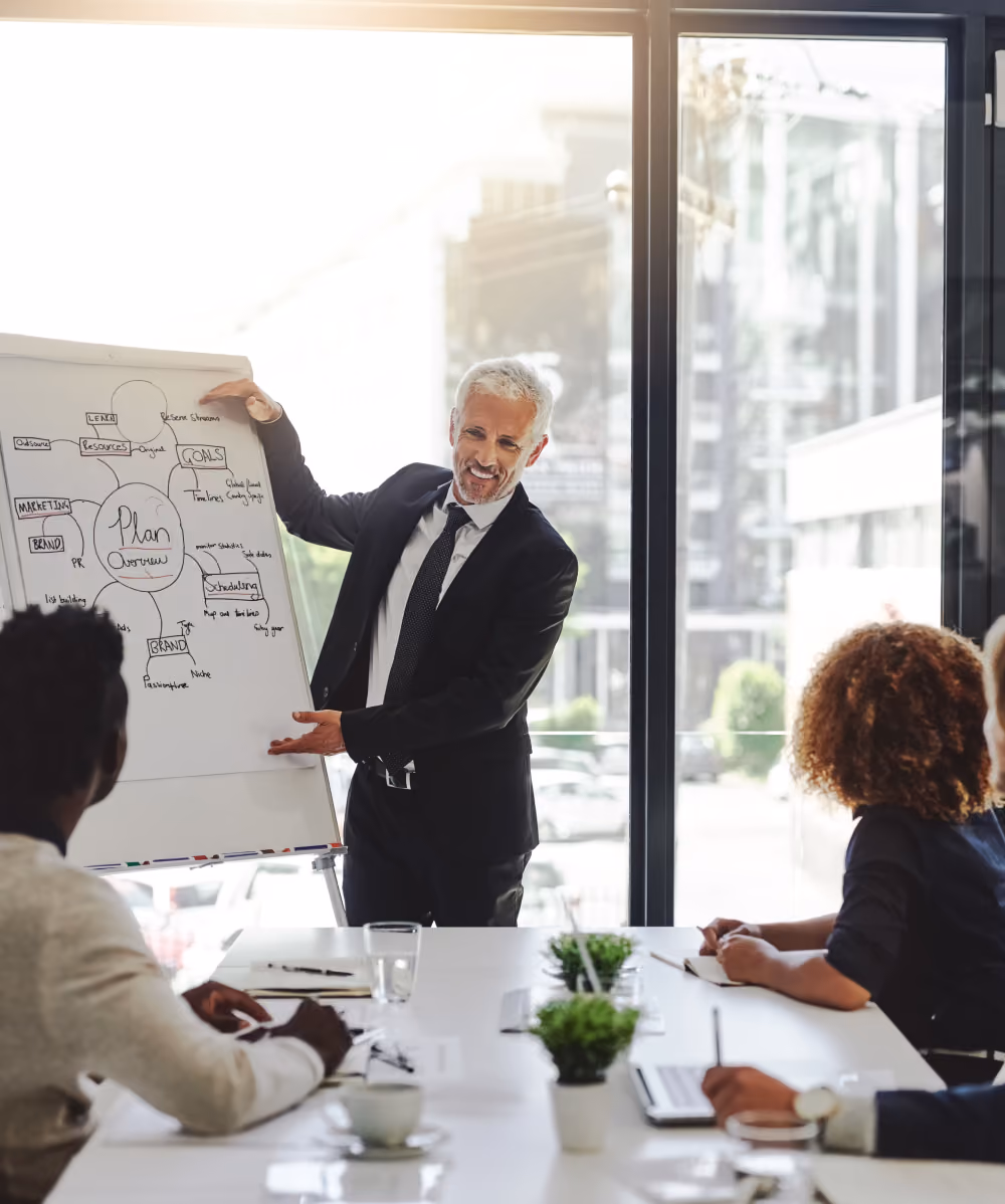 Businessman in suit presenting a plan overview on a flip chart to colleagues in a meeting room.