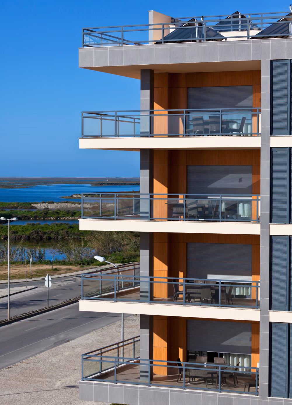 Close-up exterior view of a modern multi-story building with wood-paneled balconies overlooking a coastal waterway and marshland.