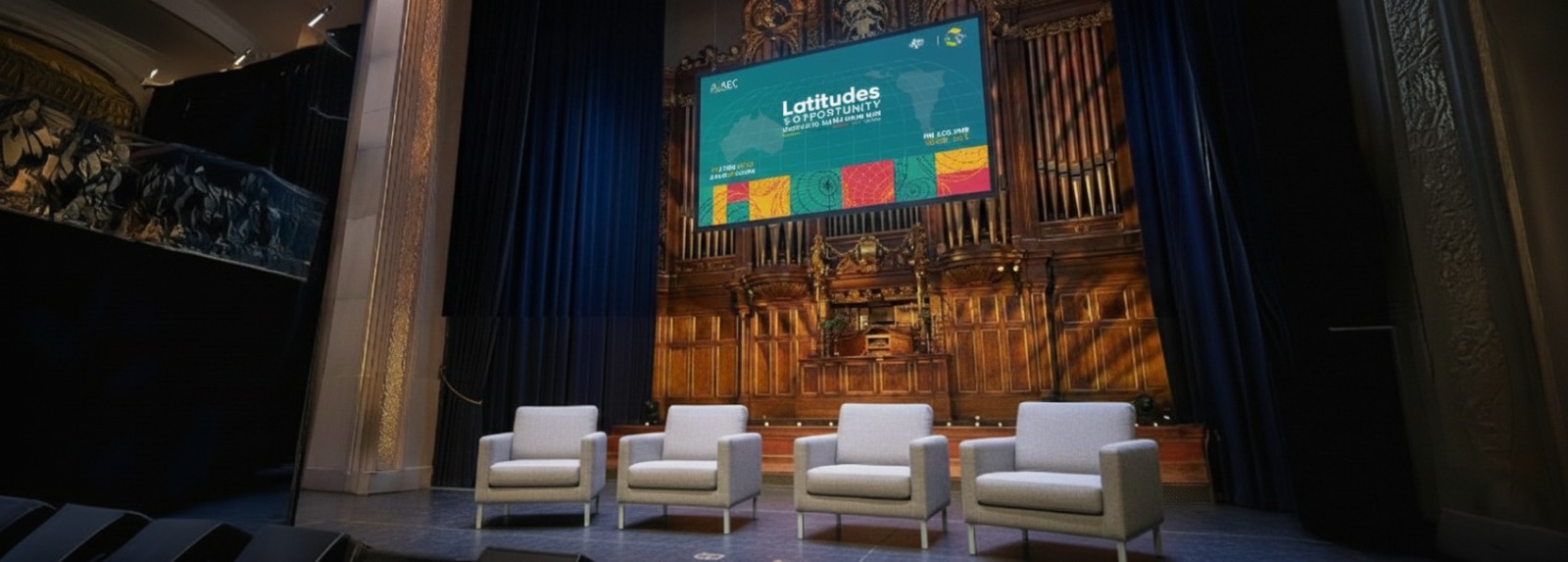 Four empty gray armchairs arranged on a stage in front of a wooden pipe organ and a screen displaying a presentation titled 'Latitudes of Opportunity'.