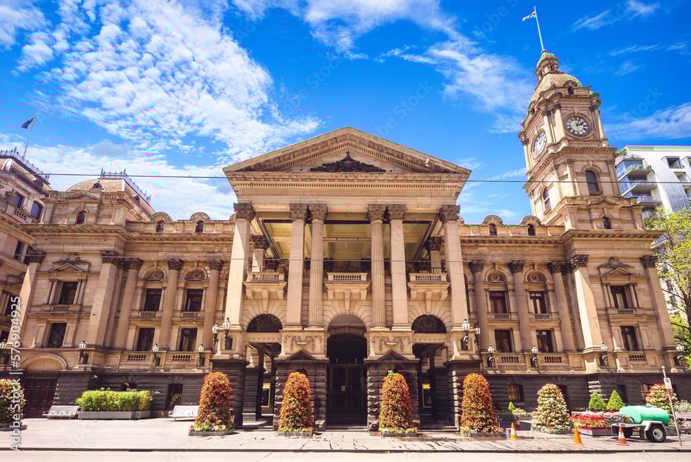 Historic sandstone building with large columns and a clock tower under a blue sky with scattered clouds.