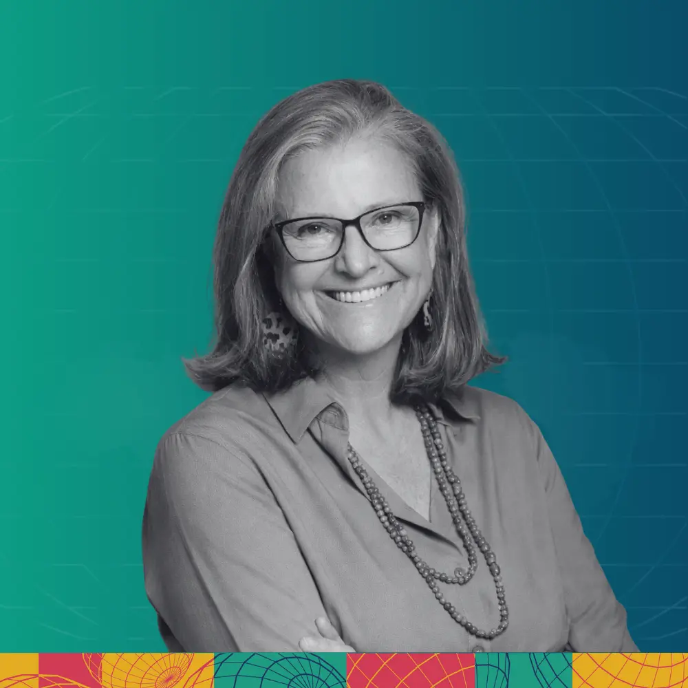 Smiling woman with glasses, shoulder-length hair, wearing a buttoned shirt and beaded necklace, against a teal and blue gradient background with geometric patterns.