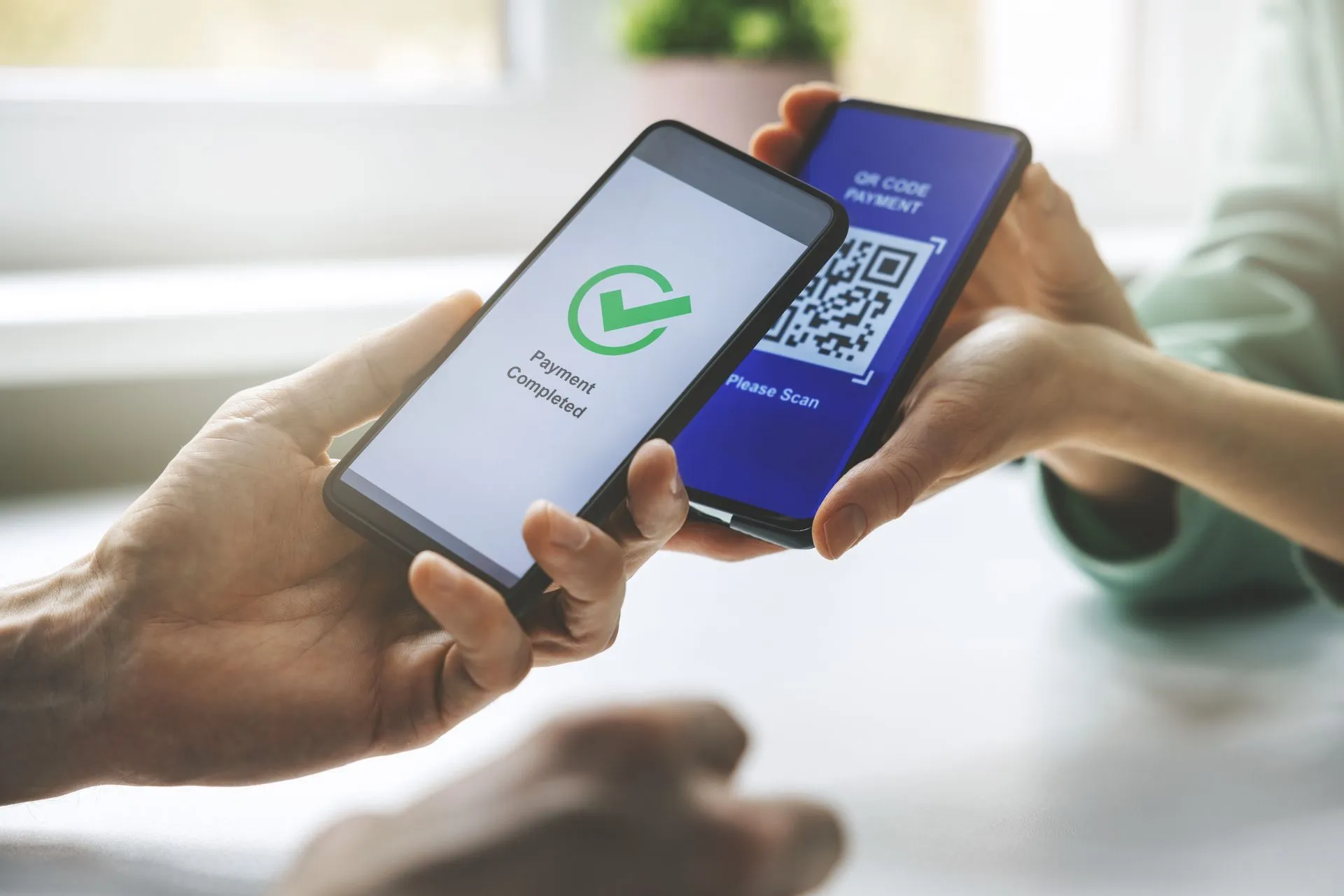 Two hands holding smartphones, one displaying a QR code for payment and the other showing a confirmation screen with a green checkmark and 'Payment Completed' text.