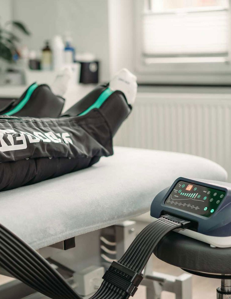 Person liegt auf Behandlungsliege und erhält Kompressionstherapie mit High-Tech-Gerät an den Beinen.