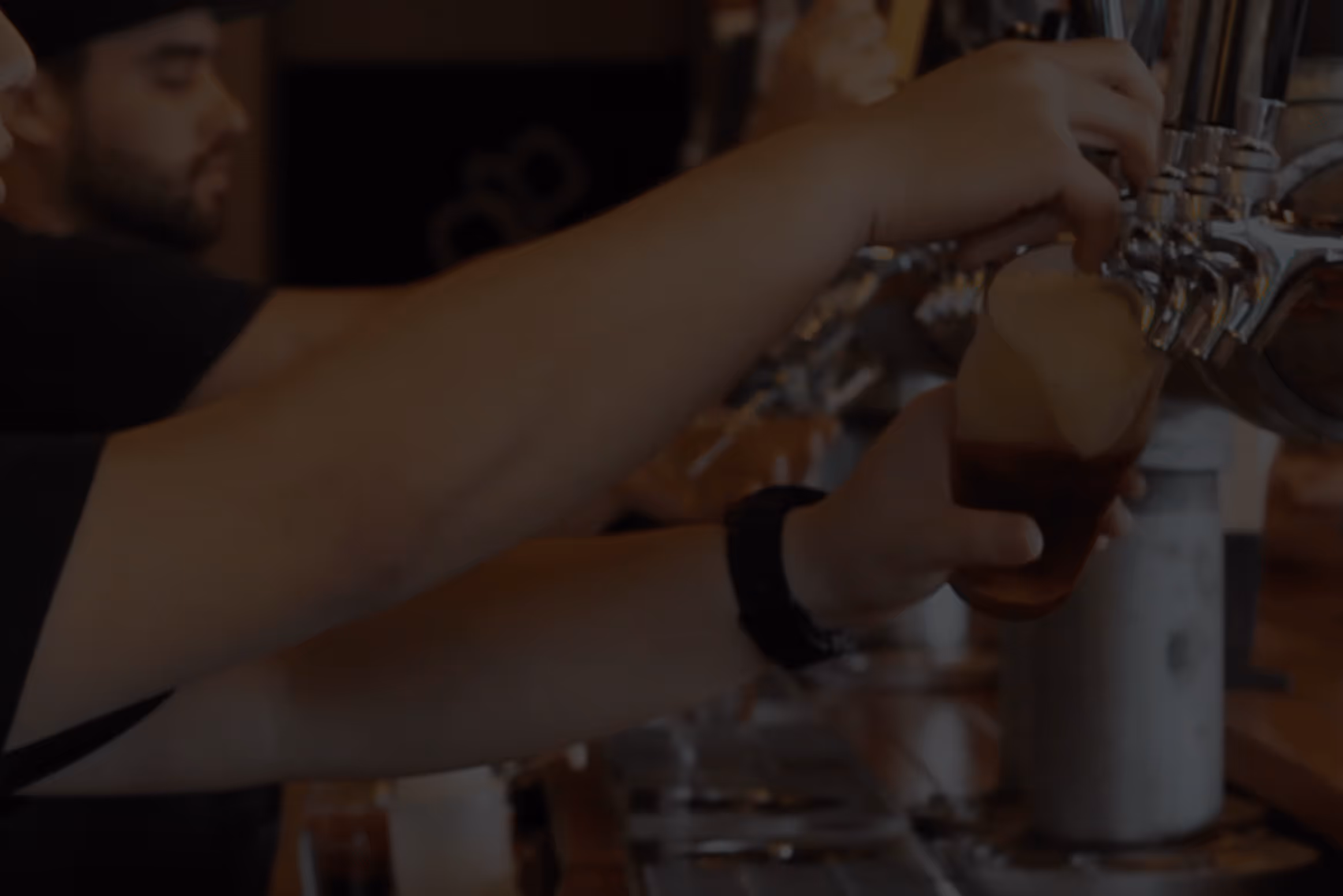 Bartender pouring a draft beer from a tap into a glass with foam head.