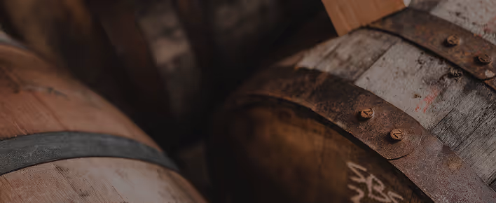 Close-up of weathered wooden barrels with metal bands in dim lighting.