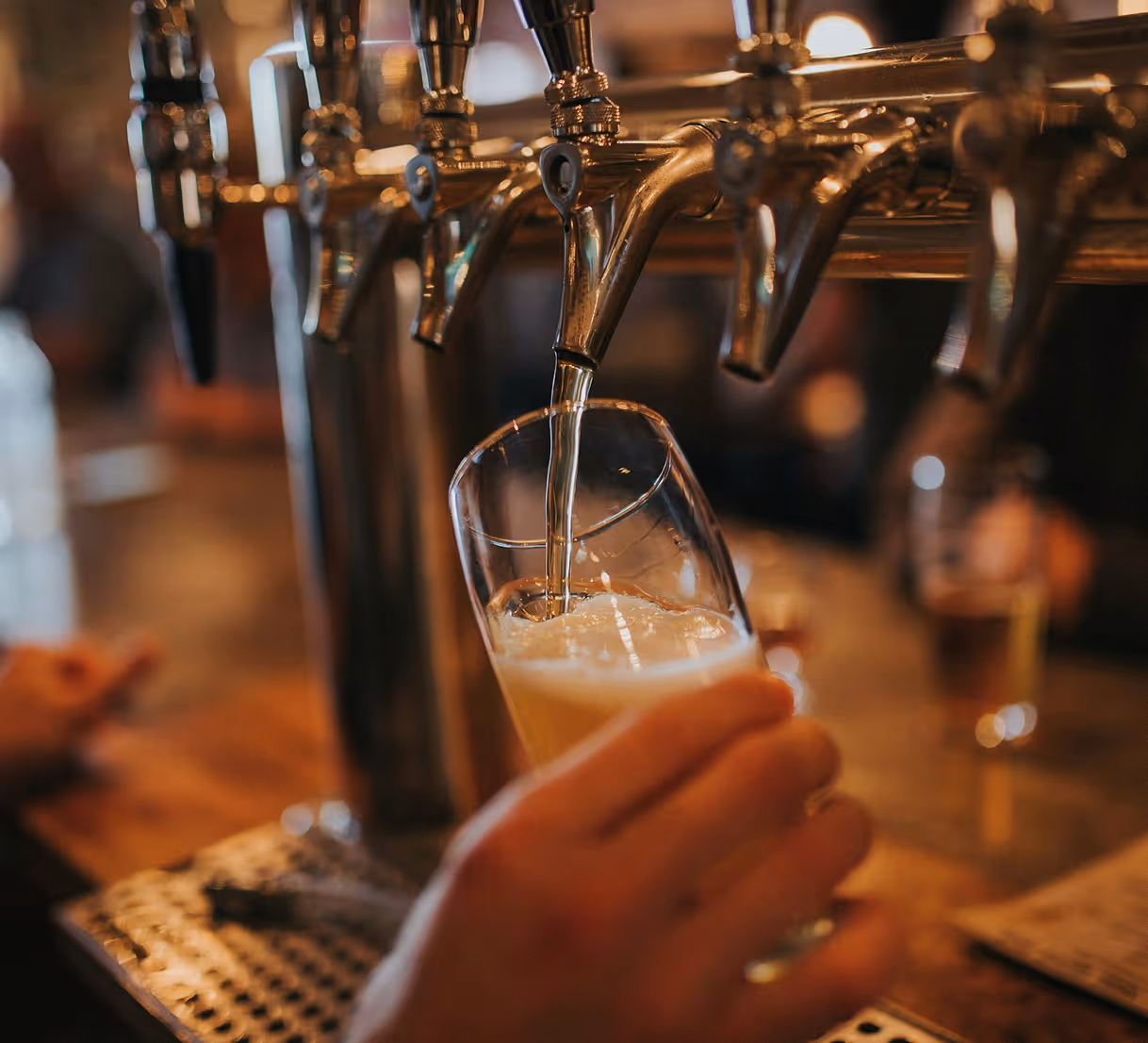 Close-up of beer being poured from a tap into a tilted glass in a bar setting.