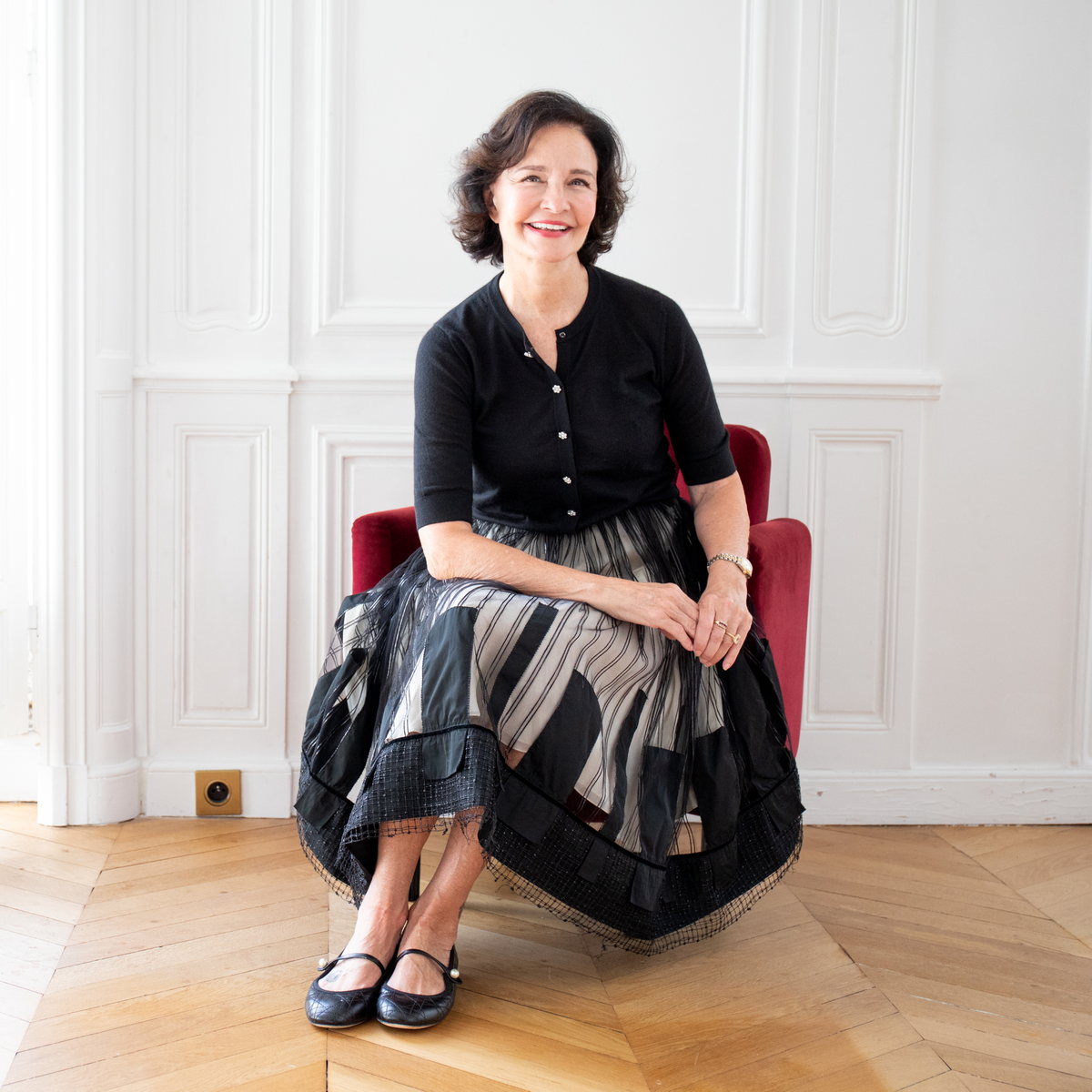 Sonia Choquette seated on a red velvet chair in her Paris apartment