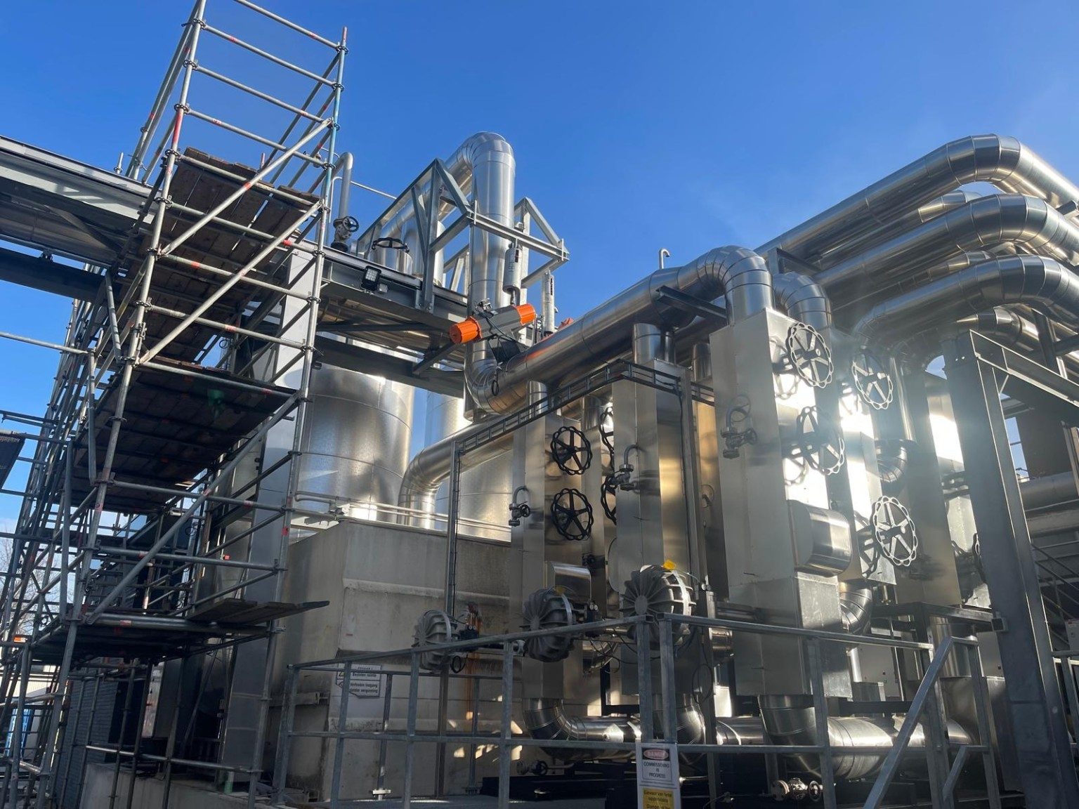 Met aluminium beplate procesleidingen en afsluiterstations bij een buiteninstallatie, met een steiger ernaast