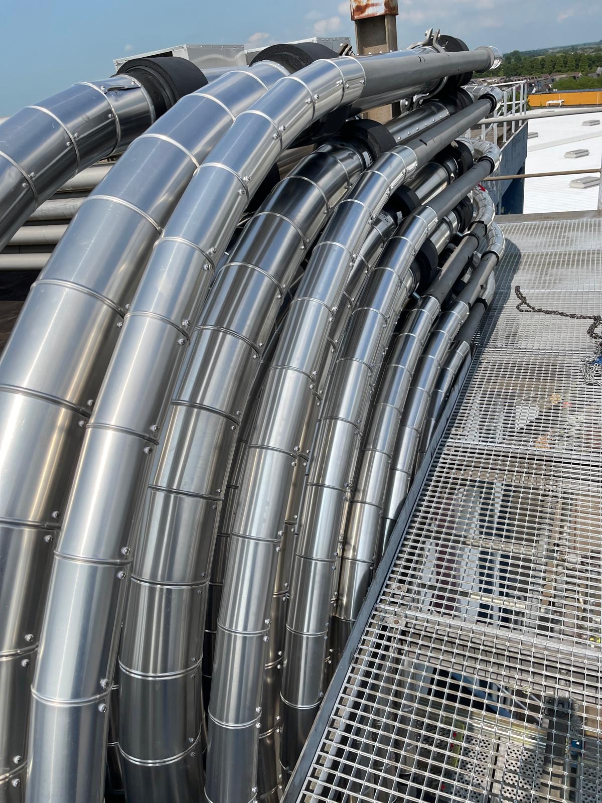 Bundel met aluminium beplate leidingen die in gesegmenteerde bochten langs een looppad op het dak lopen