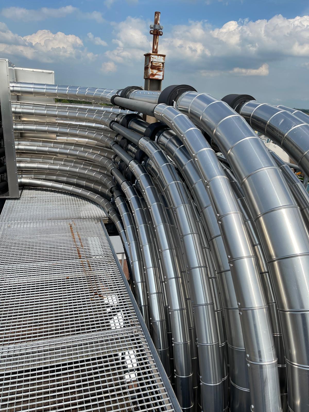 Een bundel met aluminium beplate leidingen die in gesegmenteerde bochten langs een looppad op het dak loopt