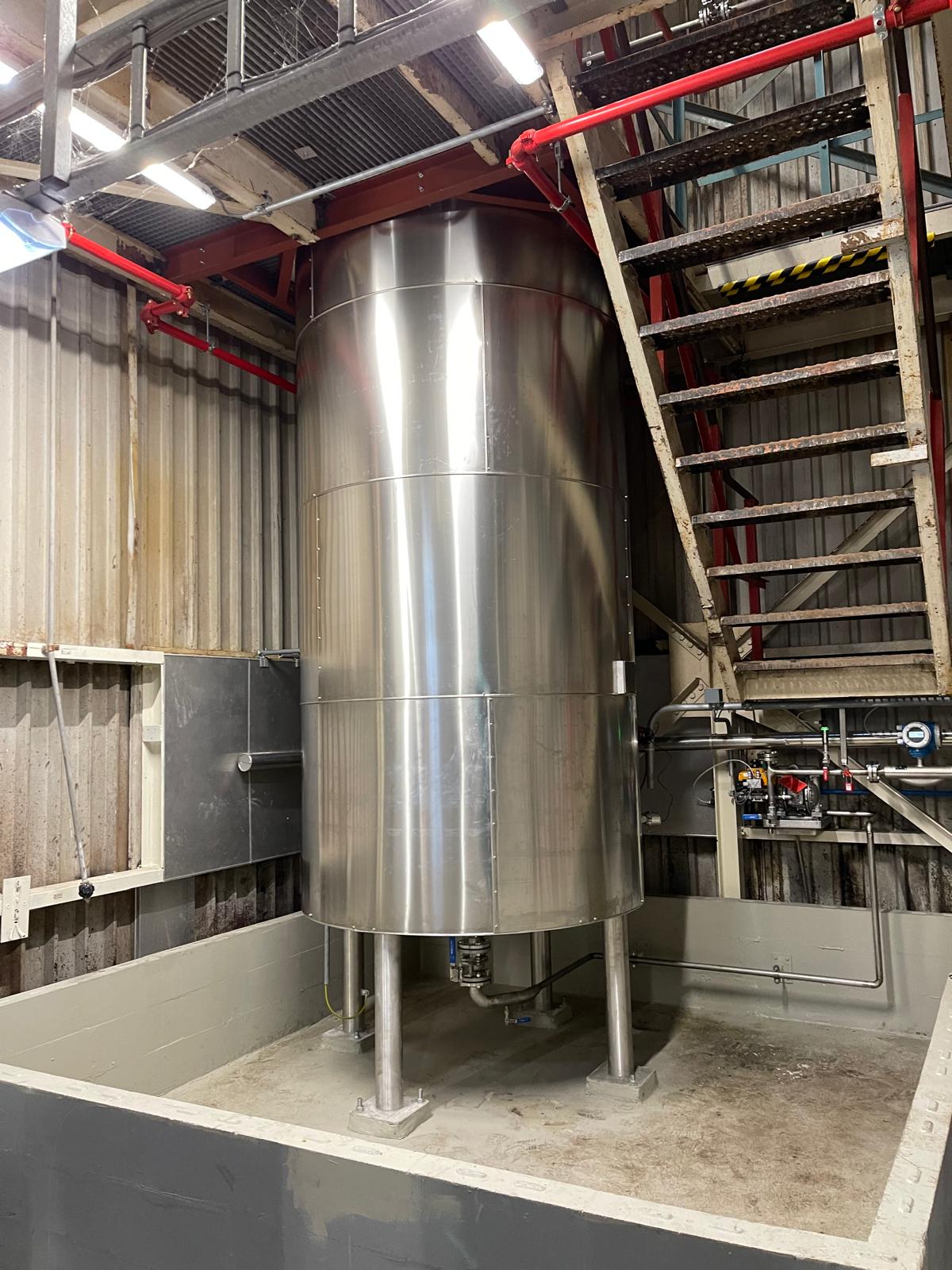 Tank afgewerkt met gesegmenteerde aluminium beplating, in de opvangbak naast een trap