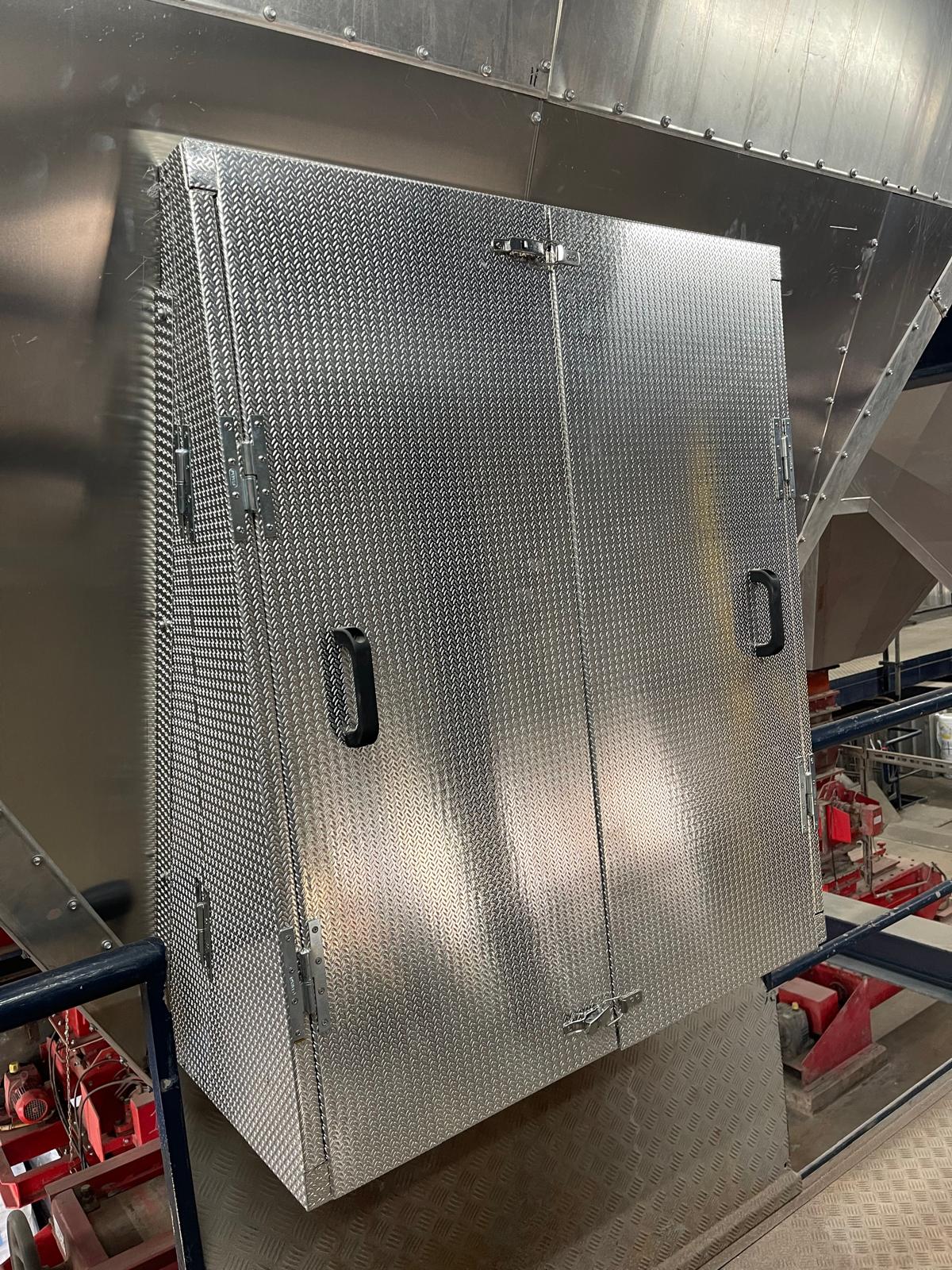 Op maat vervaardigde omkasting van aluminium tranenplaat met twee scharnierende toegangsdeuren, handgrepen en sluitingen, gemonteerd tegen beplate industriële apparatuur
