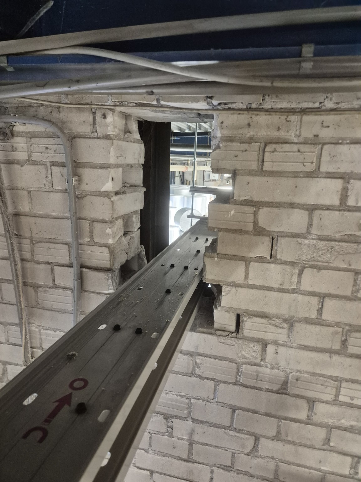 Grote onafgedichte opening in een bakstenen wand waar een kabelgoot doorheen loopt