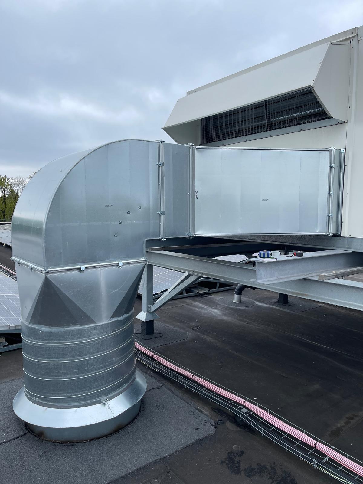 Ongeïsoleerde verzinkte rechthoekige kanaalbocht die vanaf het dak omhoog loopt naar een ventilatie-unit