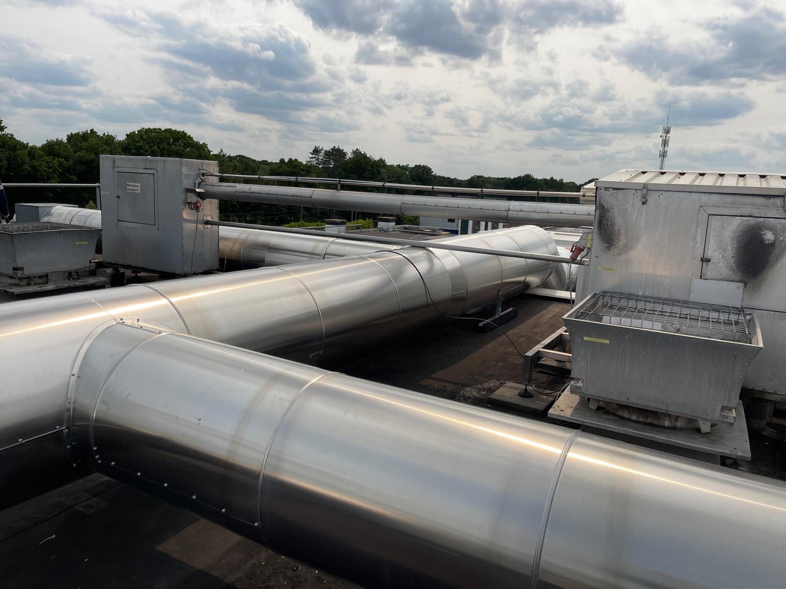 Kanalen op het dak, afgewerkt met aluminium beplating, tussen ventilatie-units op een plat dak