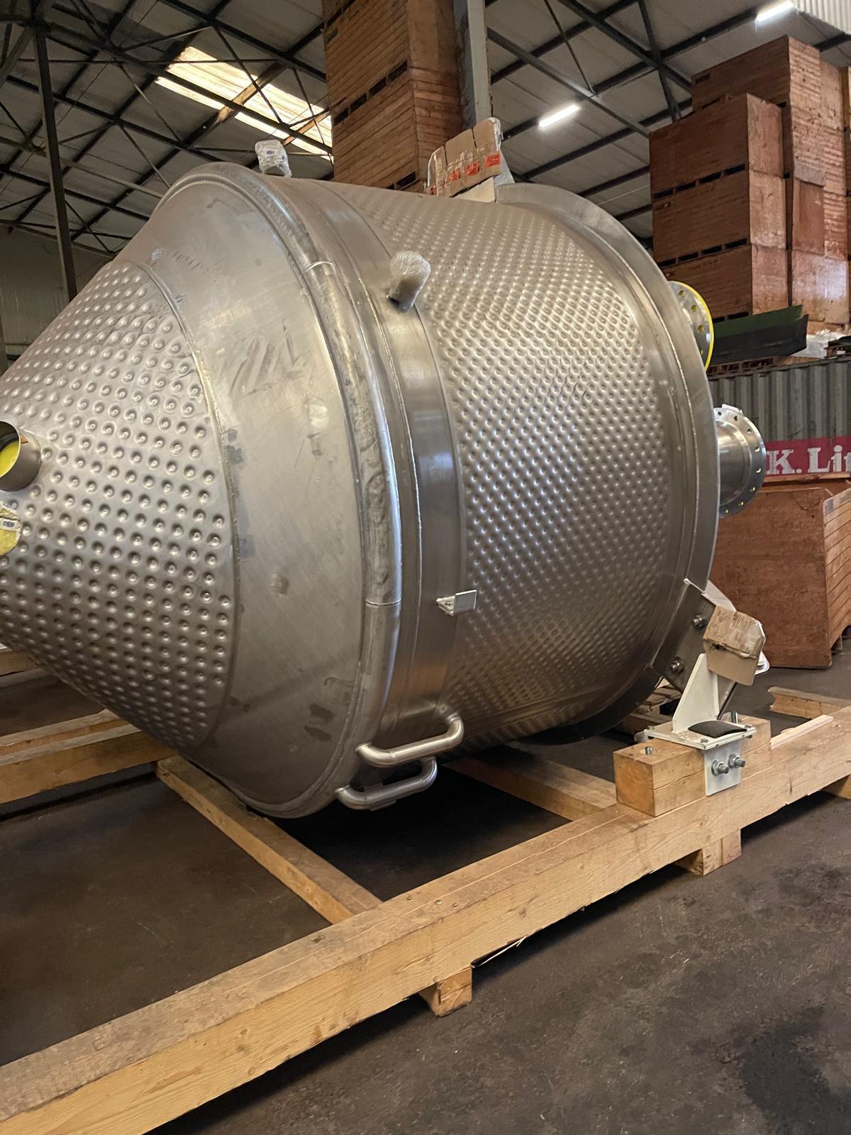 Kaal procesvat van opzij, met een noppenmantel, hijsogen en aansluitstompen, rustend op een houten frame in een werkplaats