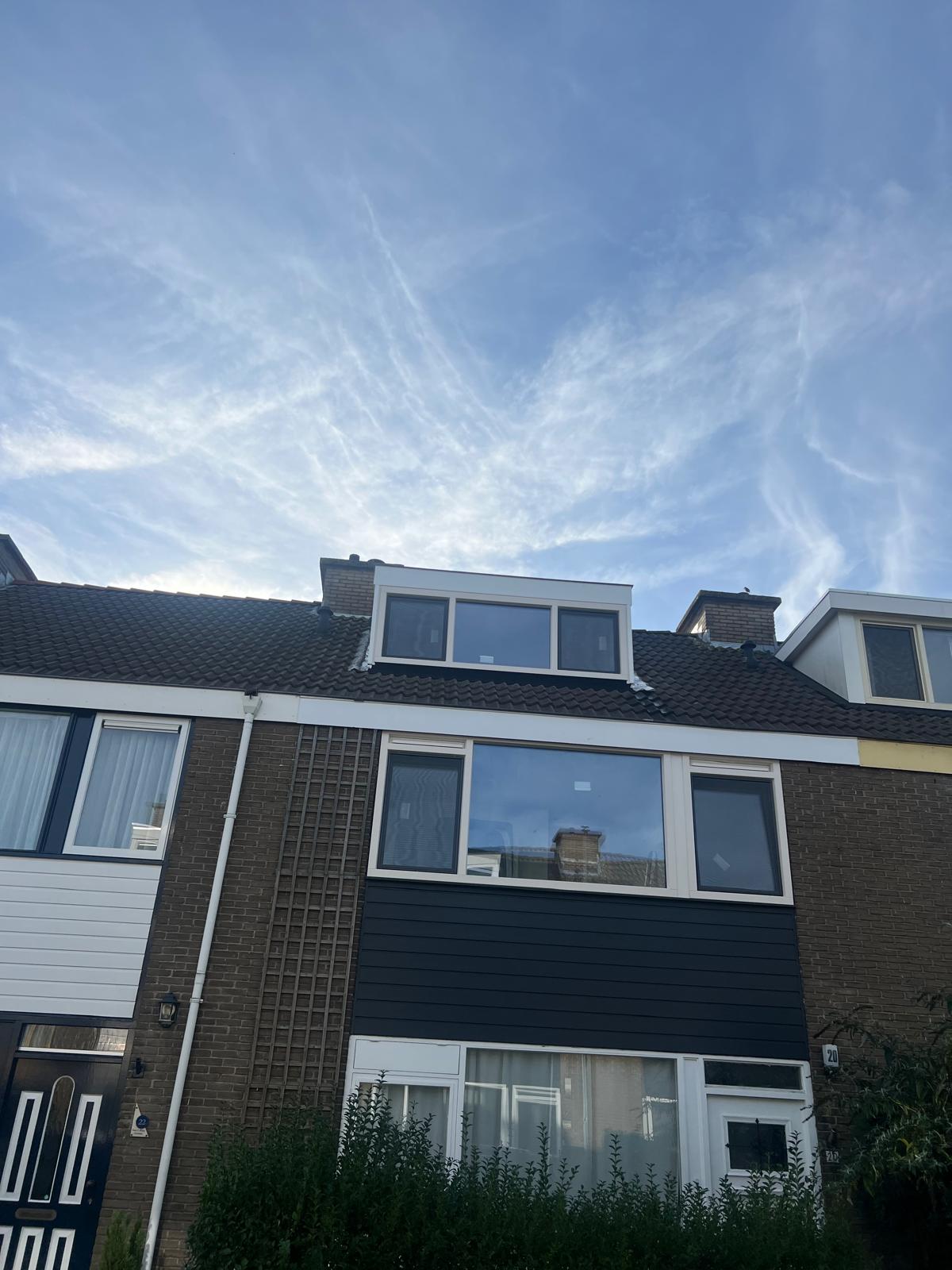 Voorgevel met nieuwe witte kozijnen, een grote glaspartij en donkere gevelbekleding na de werkzaamheden