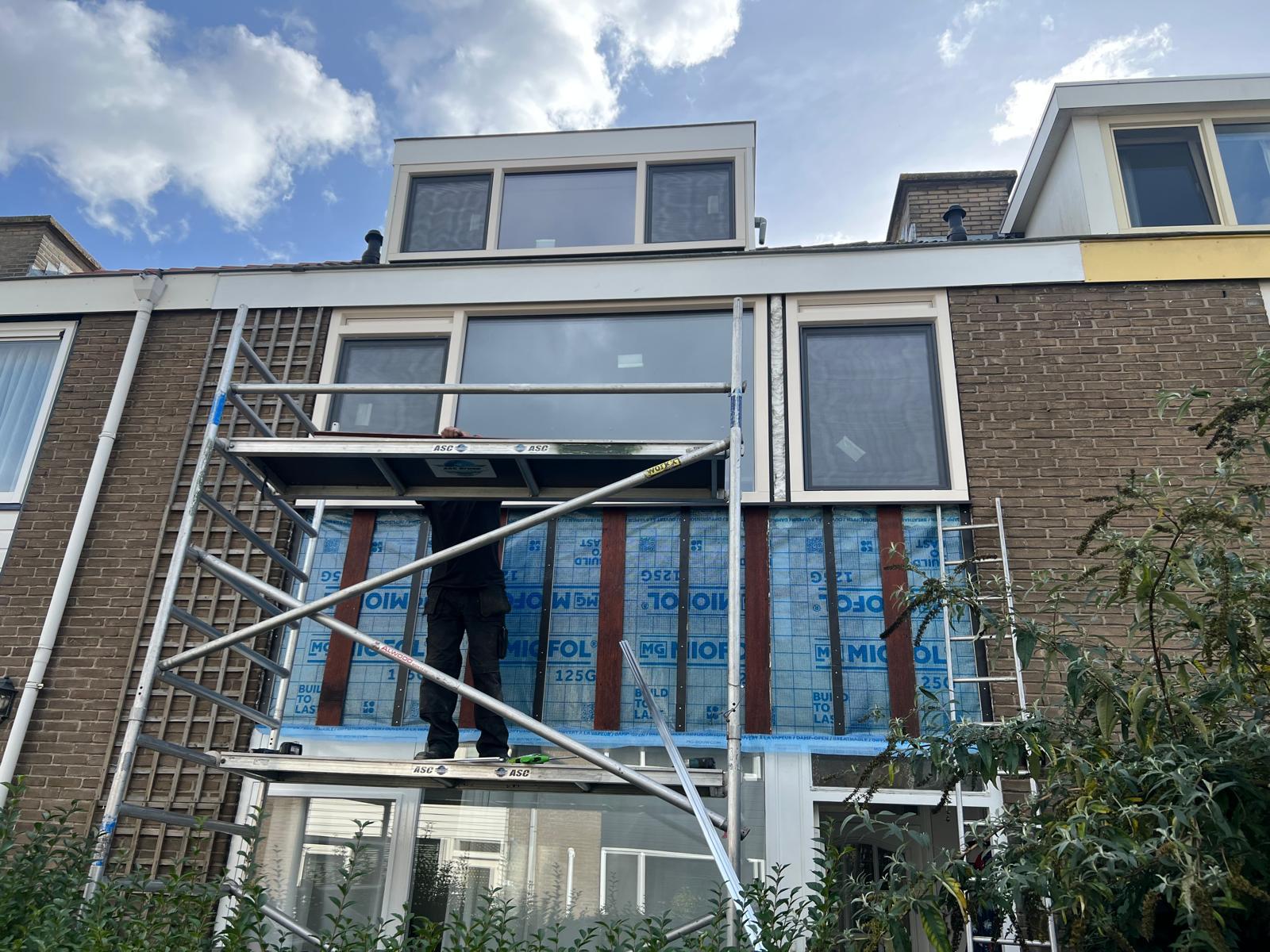 Vakman op een steiger tijdens het vervangen van de kozijnen in de voorgevel van een woning