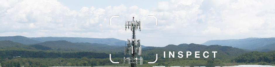 Cellular tower with multiple antennas set against a backdrop of forested hills and cloudy sky.