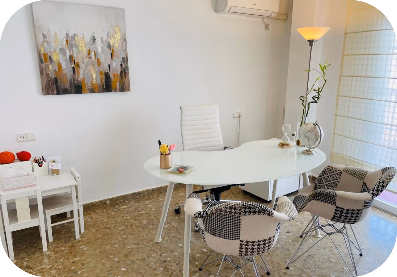 Oficina moderna con una mesa ovalada blanca, silla giratoria blanca, dos sillones de patchwork, lámpara de pie y decoración minimalista que incluye un globo terráqueo y plantas.