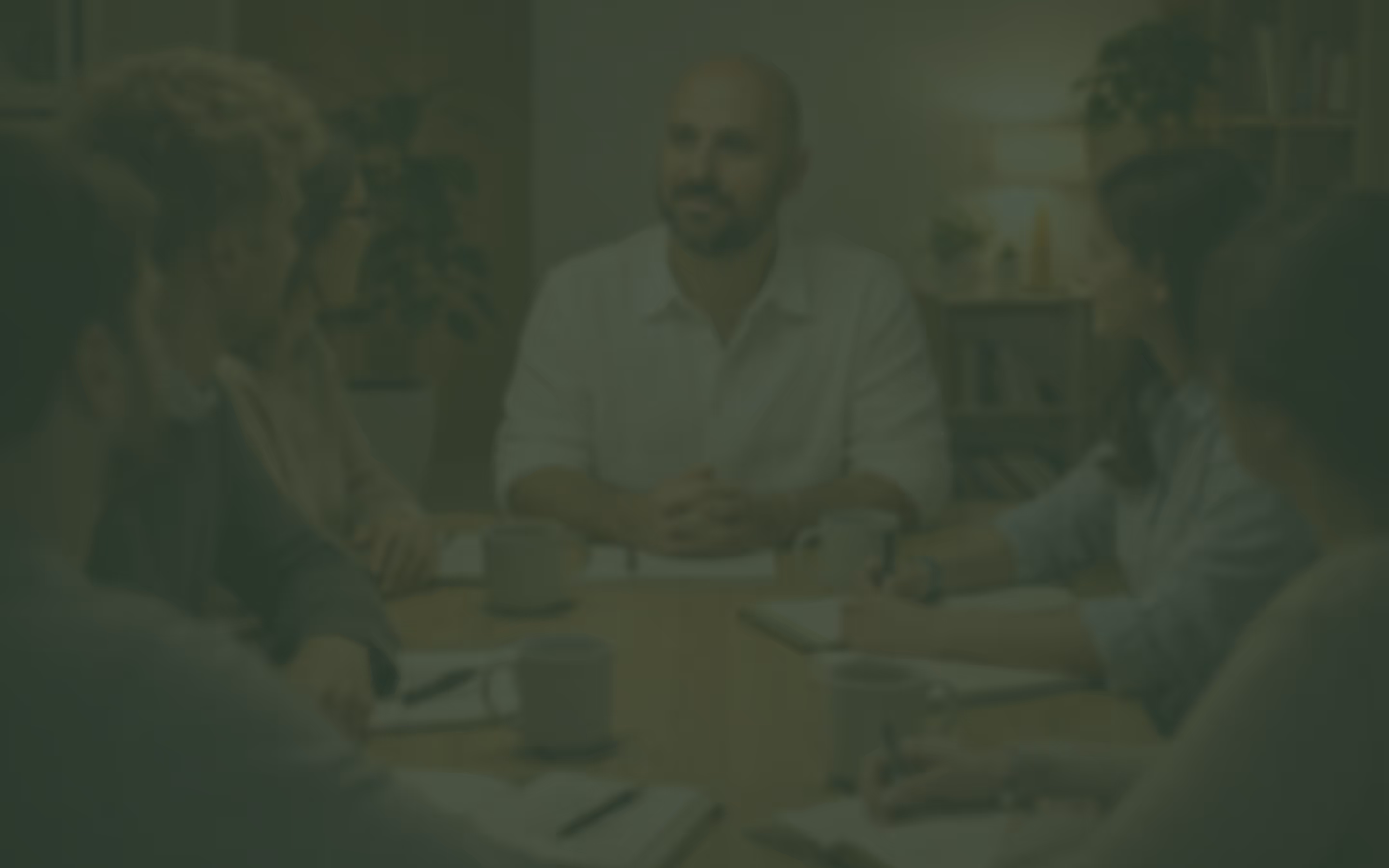Rafael, psicólogo, durante una sesión de supervisión de psicoterapia. Está con otras personas sentadas alrededor de una mesa participando en una discusión, con cuadernos y tazas de café sobre la mesa.