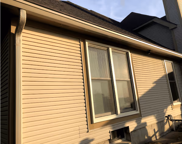 Side of a beige house with horizontal vinyl siding, two windows, and a white downspout.