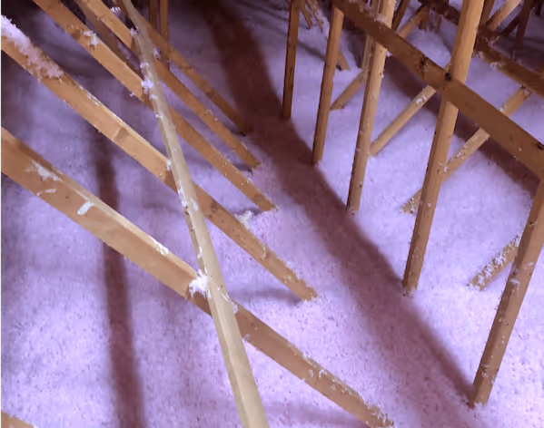Attic with wooden beams and floor covered in white loose-fill insulation material.