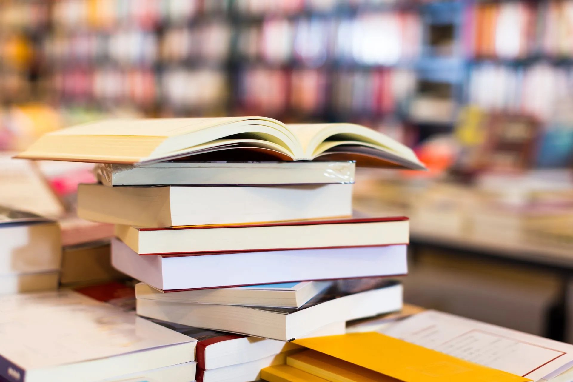 Stack of books on a table with an open book on top in a blurred bookstore background.