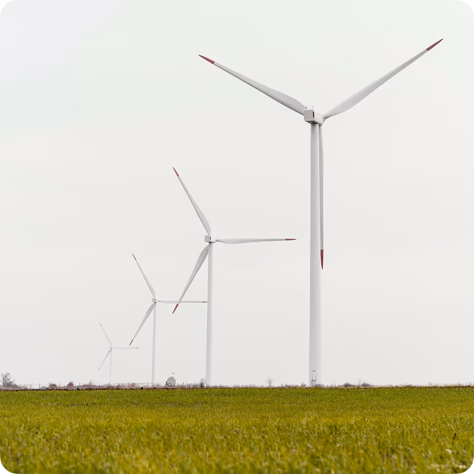 Four large white wind turbines with red tips aligned in a row on green grass under an overcast sky.