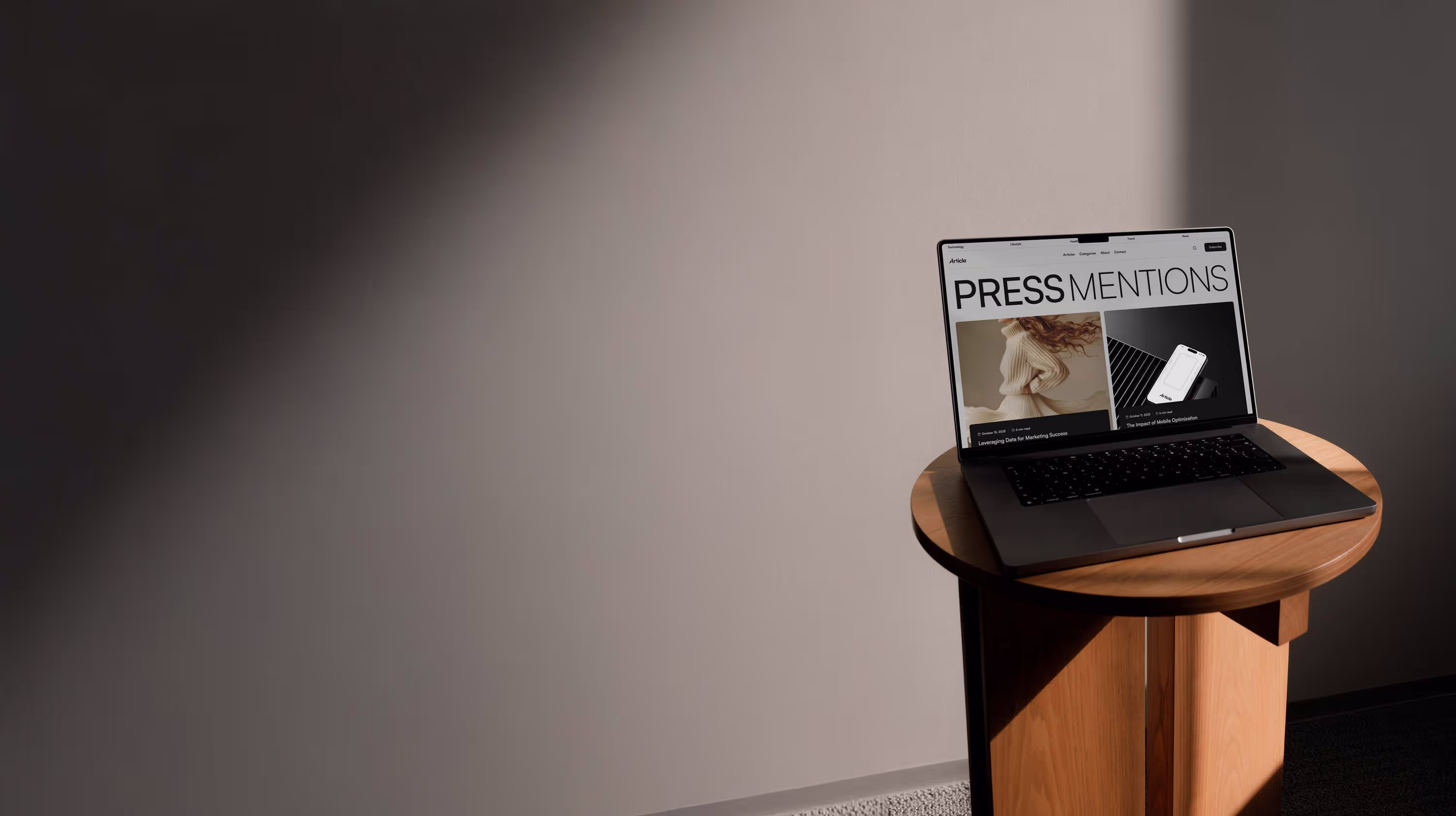Laptop displaying a webpage titled PRESS MENTIONS on a round wooden table against a plain wall.