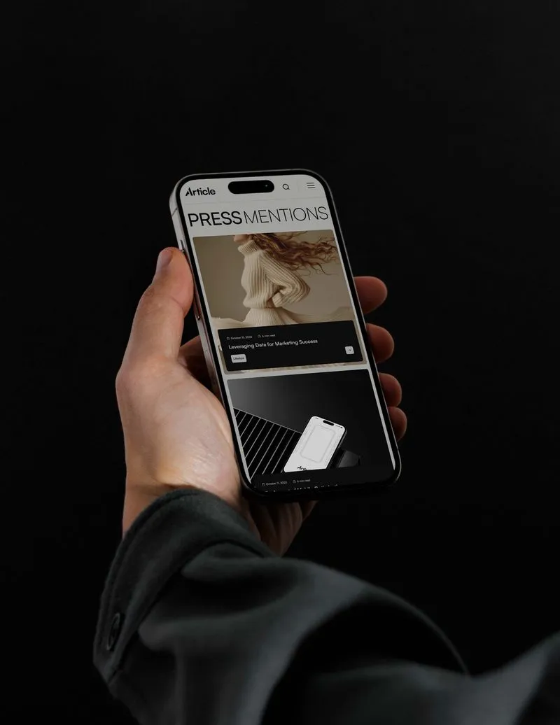 Hand holding a smartphone displaying an article titled 'PRESS MENTIONS' with images and text on a dark background.