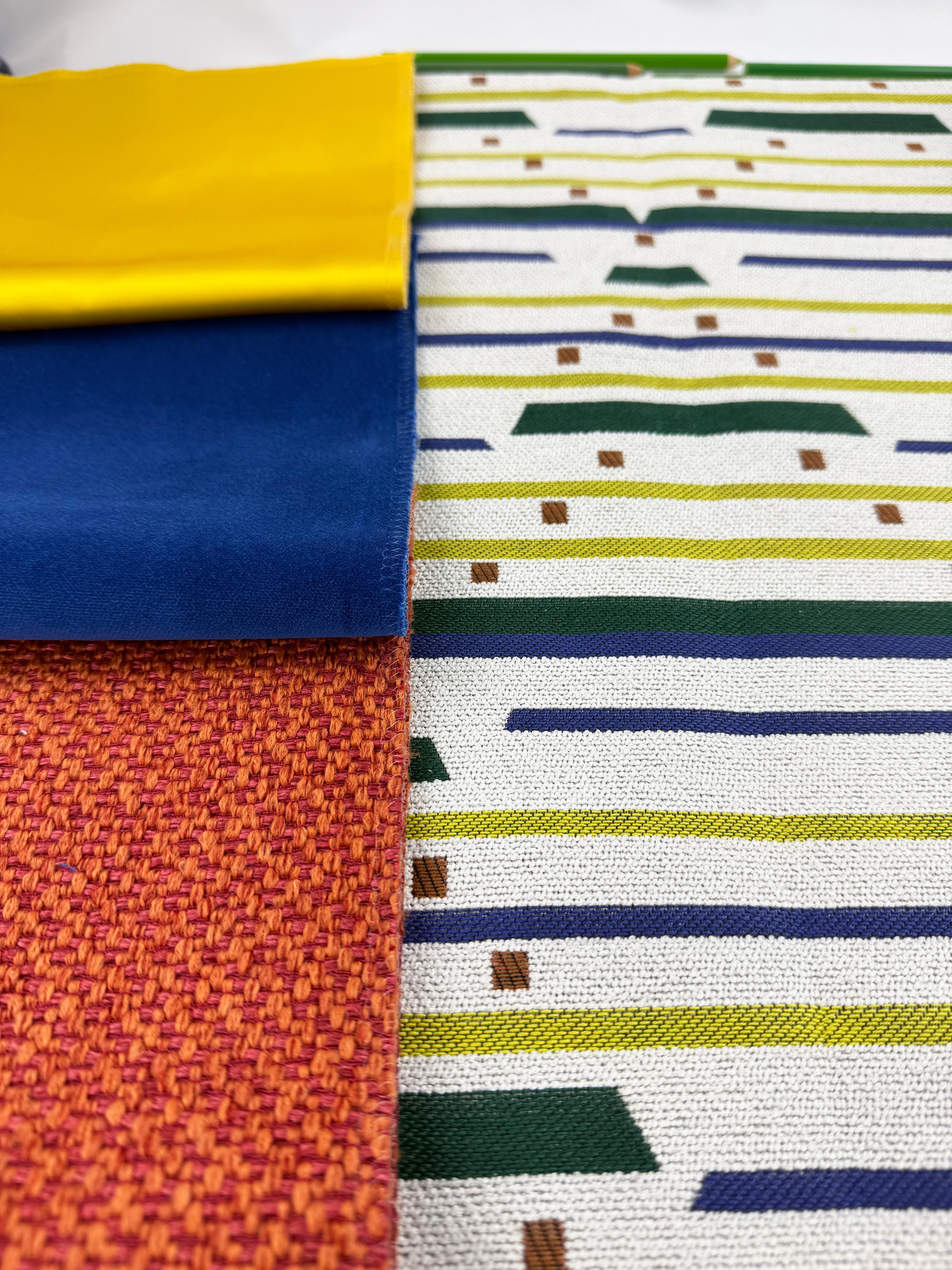 Close-up of various fabric swatches including solid yellow and blue, orange woven texture, and a patterned fabric with stripes and small geometric shapes.