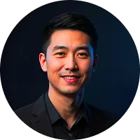 Smiling young Asian man in a black suit jacket against a dark gradient background.