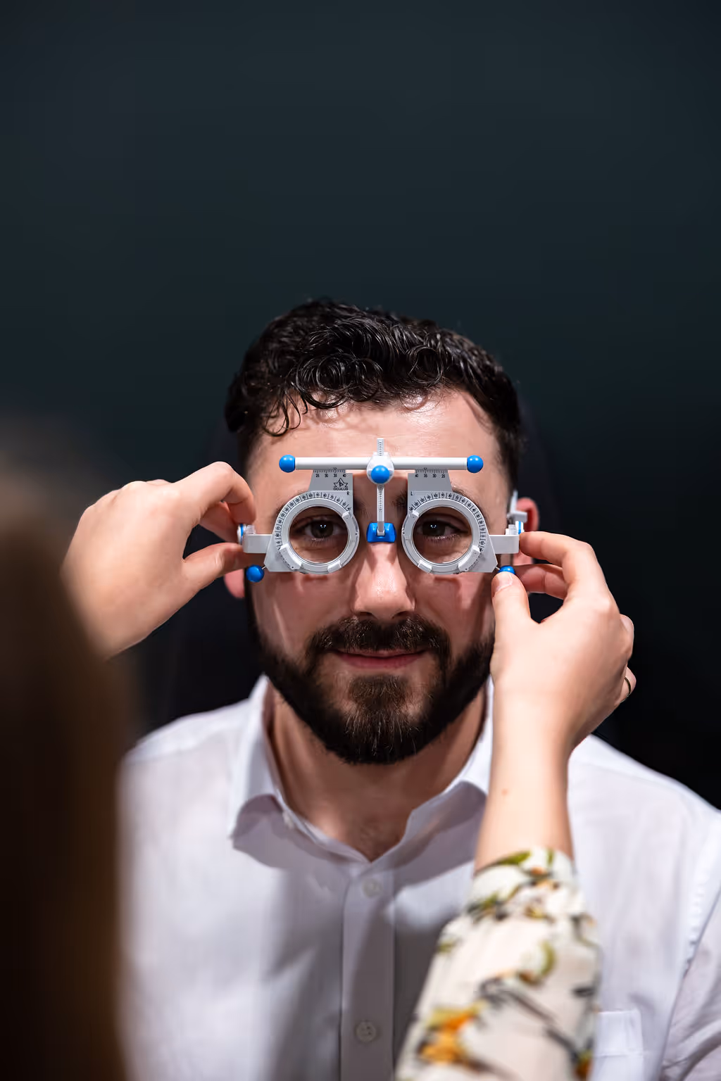 Optometrist using trial frame for eye exam against dark background