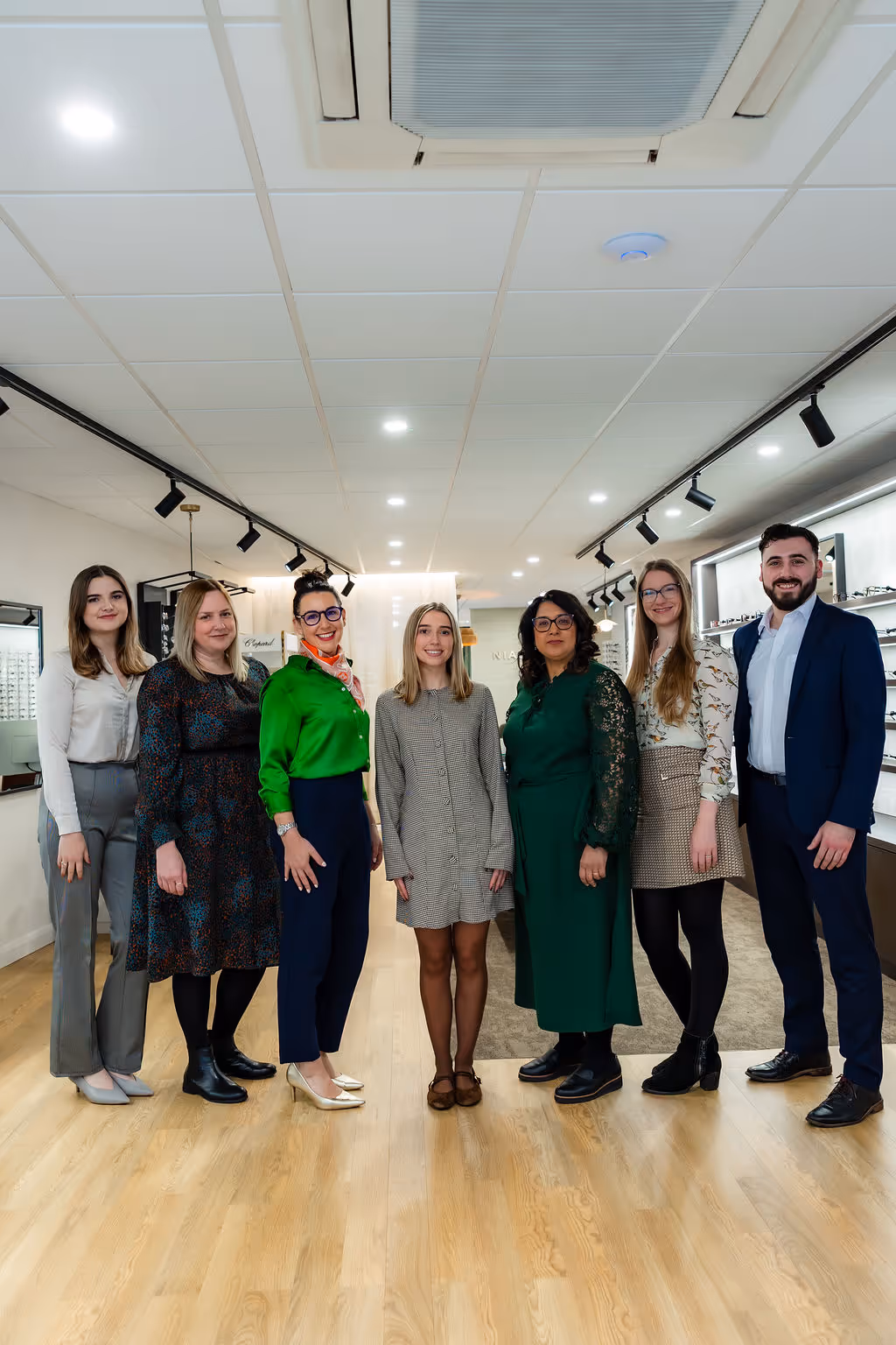 Professional team of seven posing together in an office with optical displays