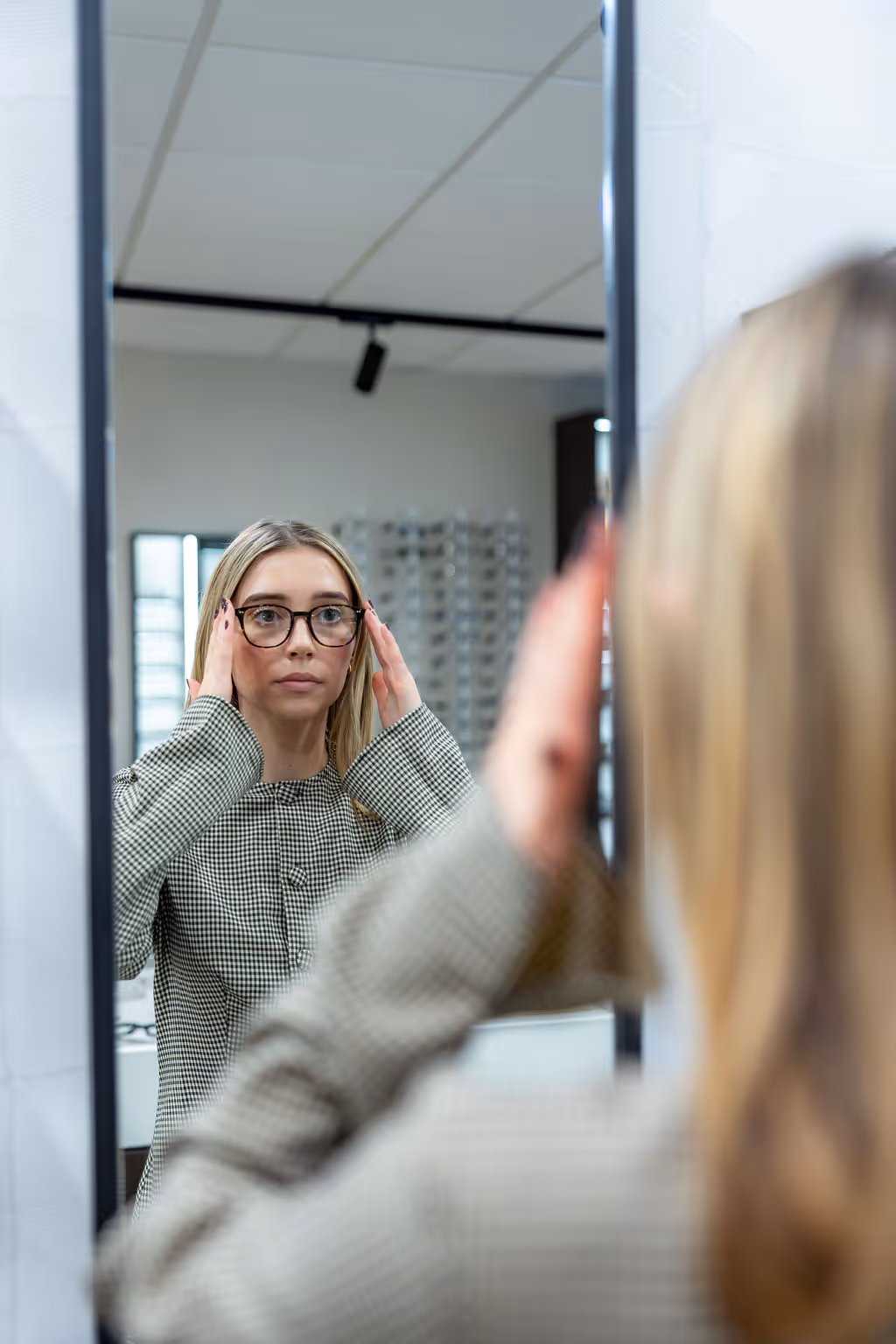 Person adjusting glasses while looking in mirror at optical store