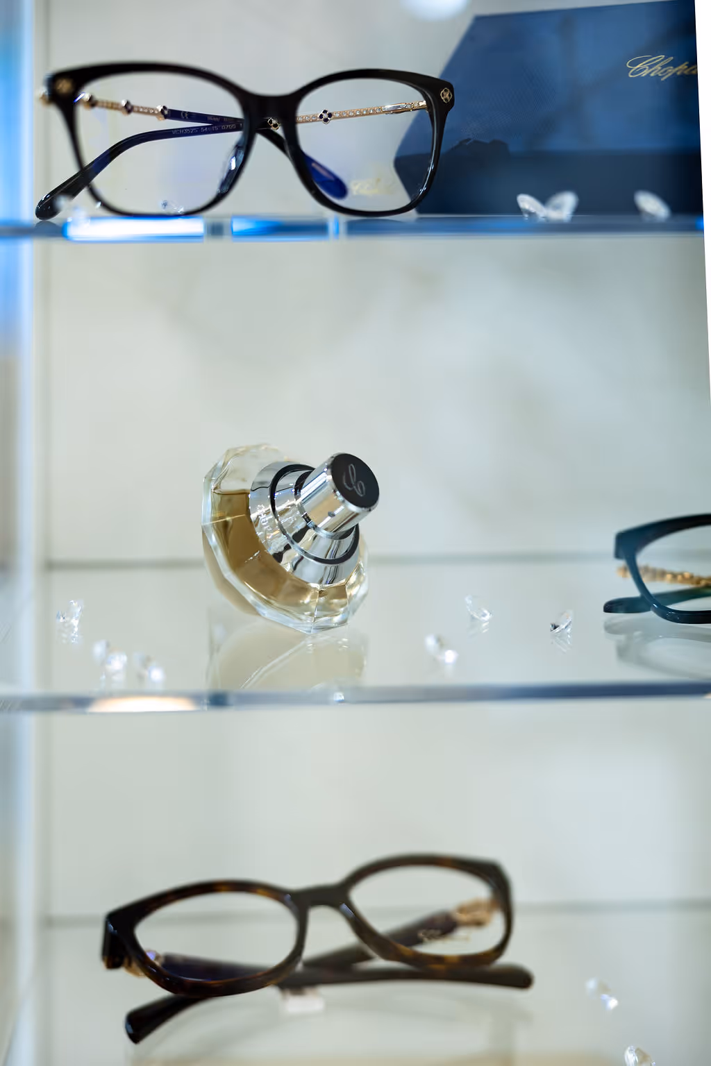Eyeglasses and perfume bottle displayed on white shelves in a store