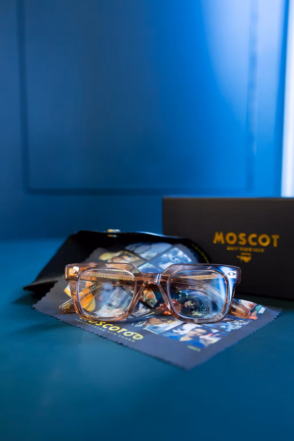 Transparent Moscot glasses on brand packaging with blue background