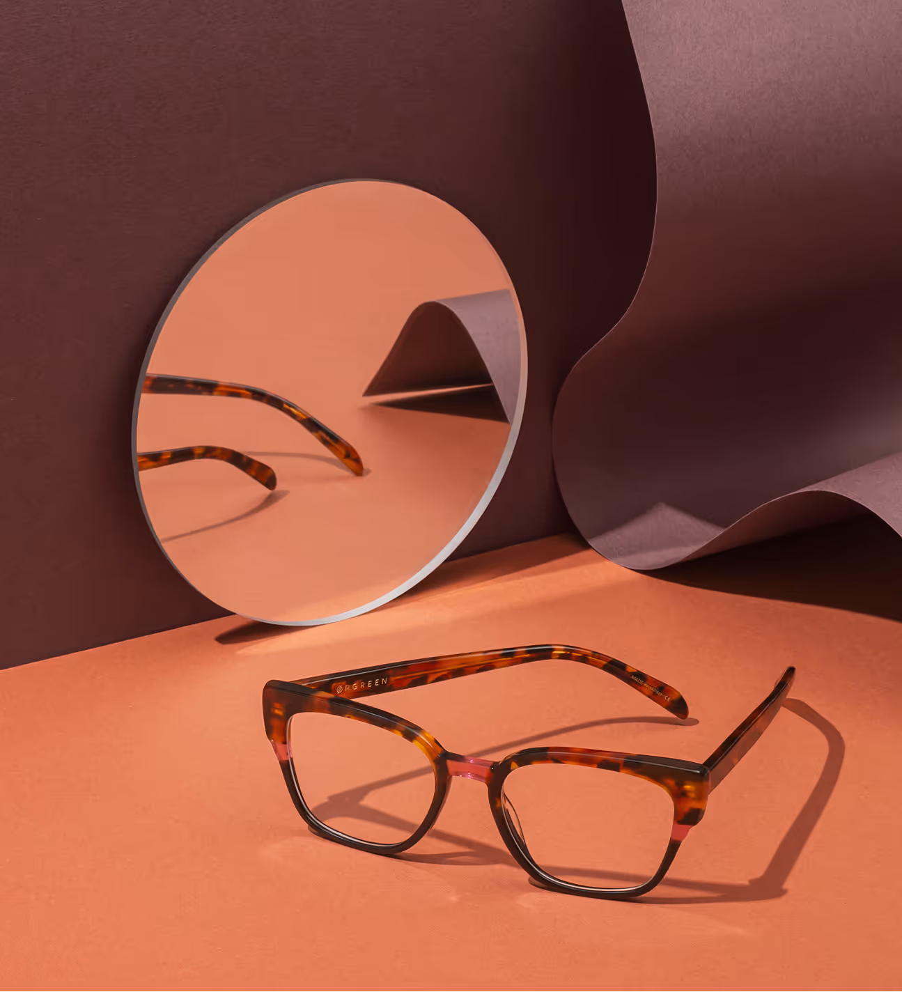 Tortoiseshell eyeglasses with reflection in round mirror on coral background