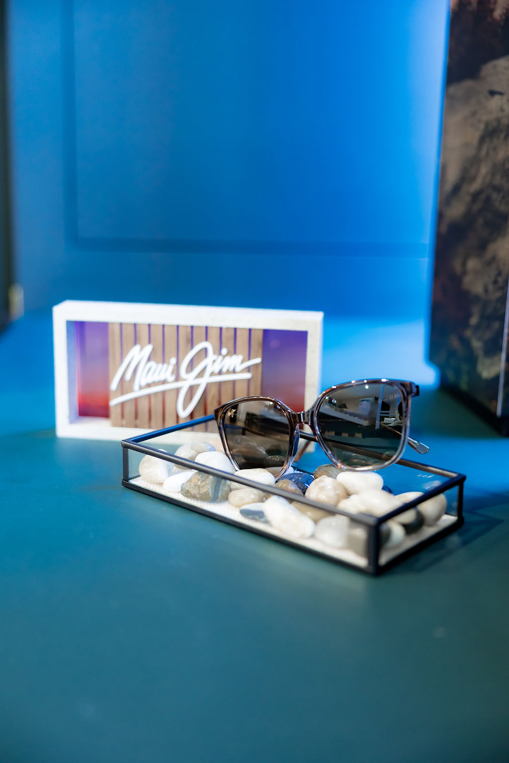 Maui Jim sunglasses on a white box with stones against blue background