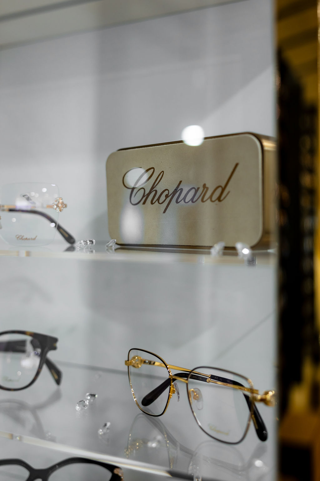 Chopard eyeglasses display with gold-rimmed glasses on a reflective surface
