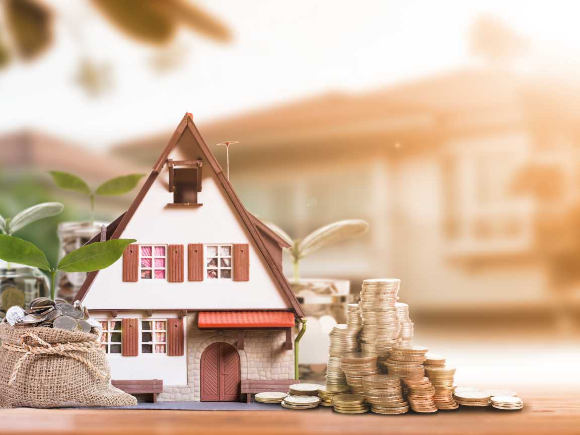 House model surrounded by coins and coin bags with leaves, symbolizing vacation rental property investment and financial planning.