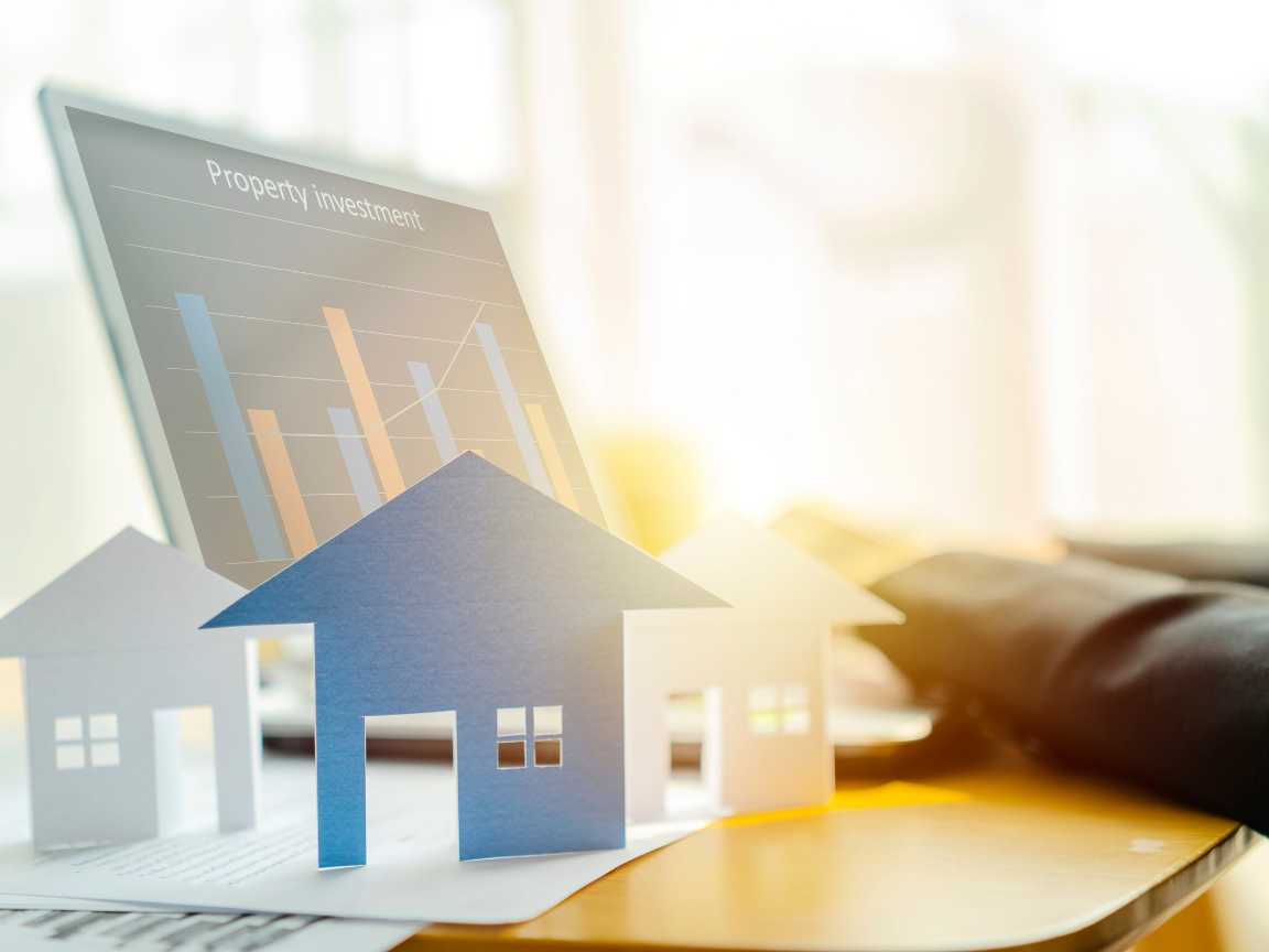 A person evaluating property investment on a laptop, with cardboard house models on the table.