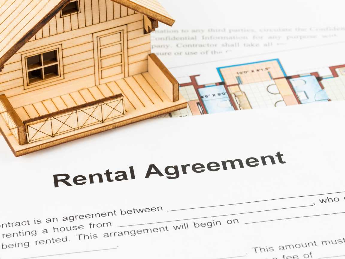 A rental agreement placed on the table next to a wooden house model.