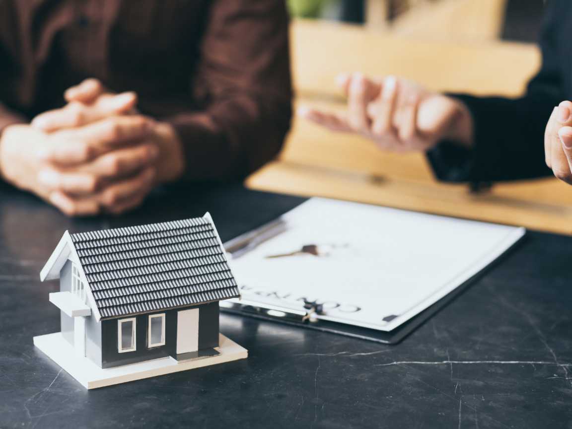 Two people discussing a property management contract with a small house model on the table.
